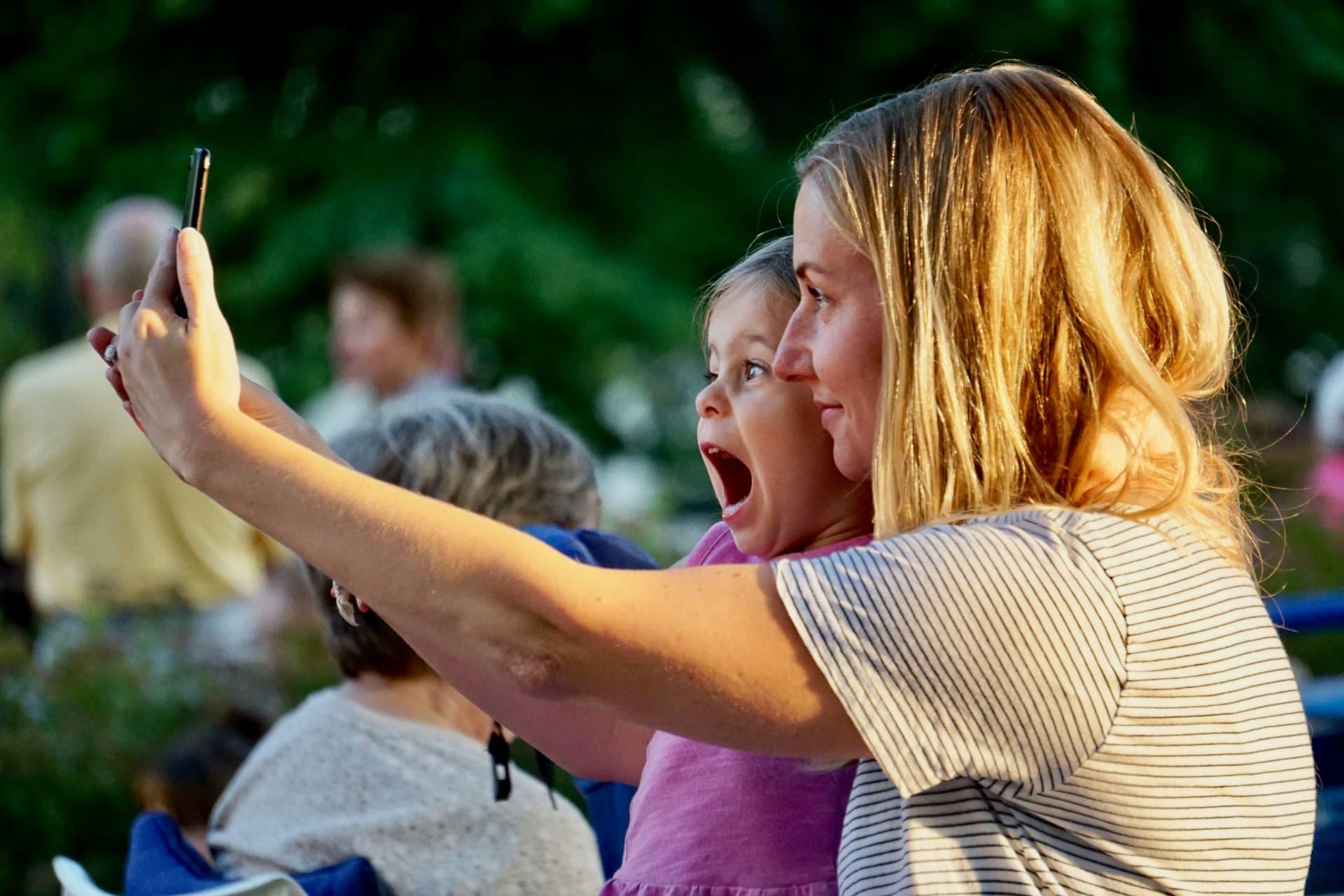 Mother and young daughter taking a selfie together at an outdoor family event
